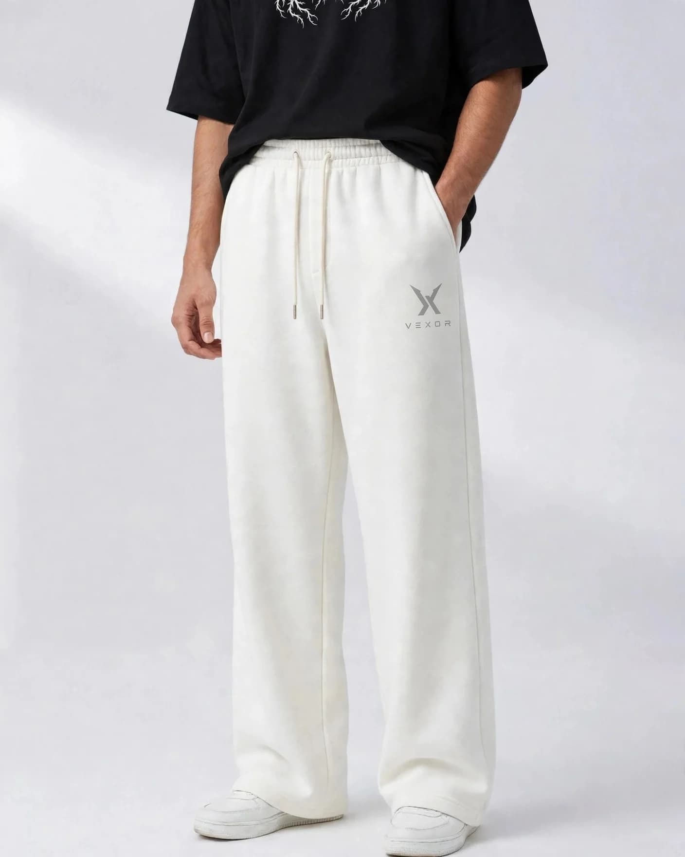 Man wearing white VEXOR wide-leg sweatpants, front view with the small light grey X logo and VEXOR name on the left thigh