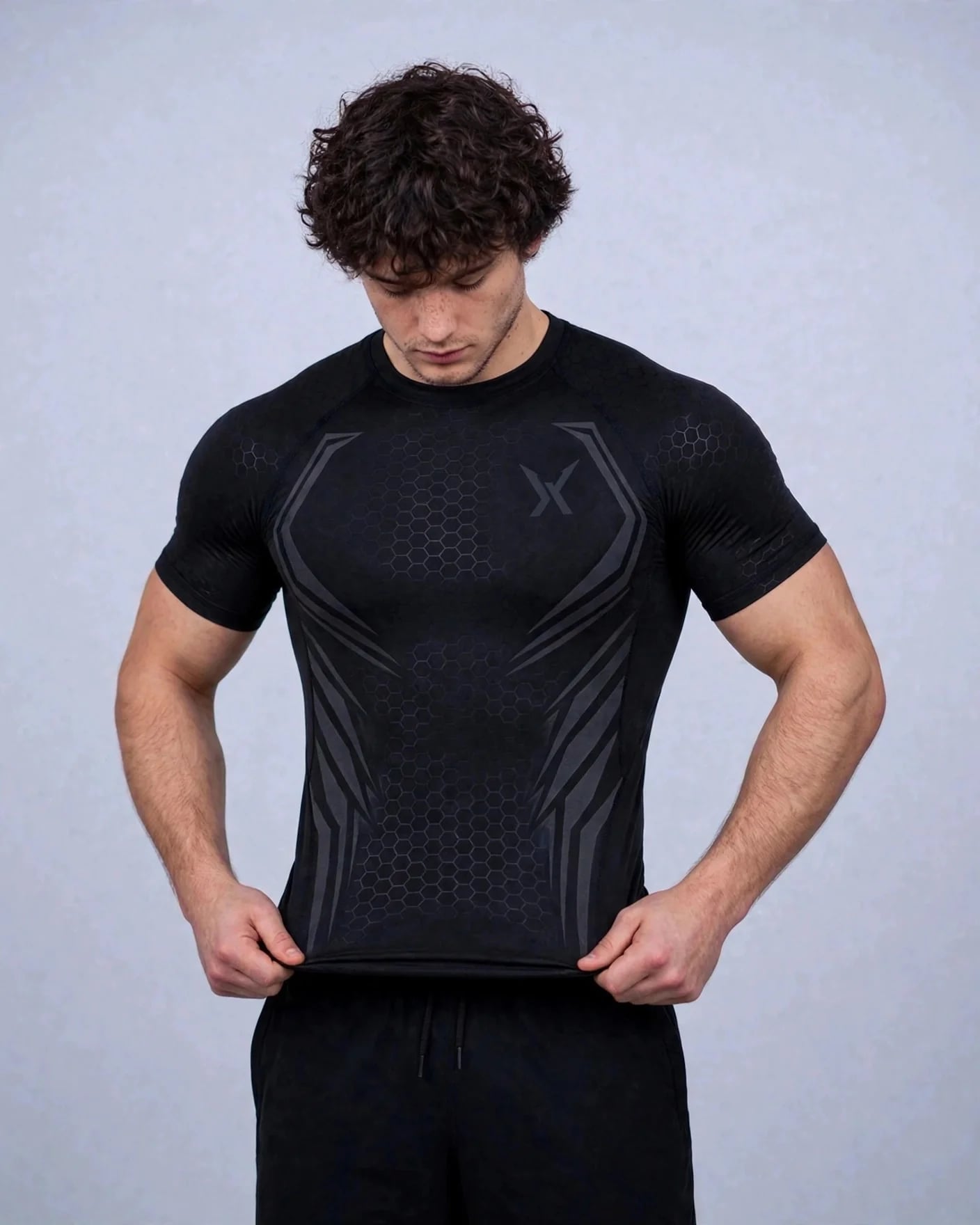 Man pulling down the hem of the black VEXOR Hex compression tee, showing the stretch fit
