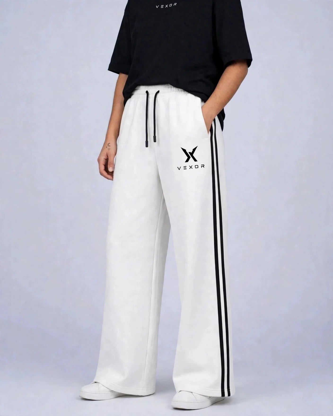 Woman wearing white VEXOR double-stripe wide-leg sweatpants with two black side stripes, front view with the small black X logo and VEXOR name on the left thigh
