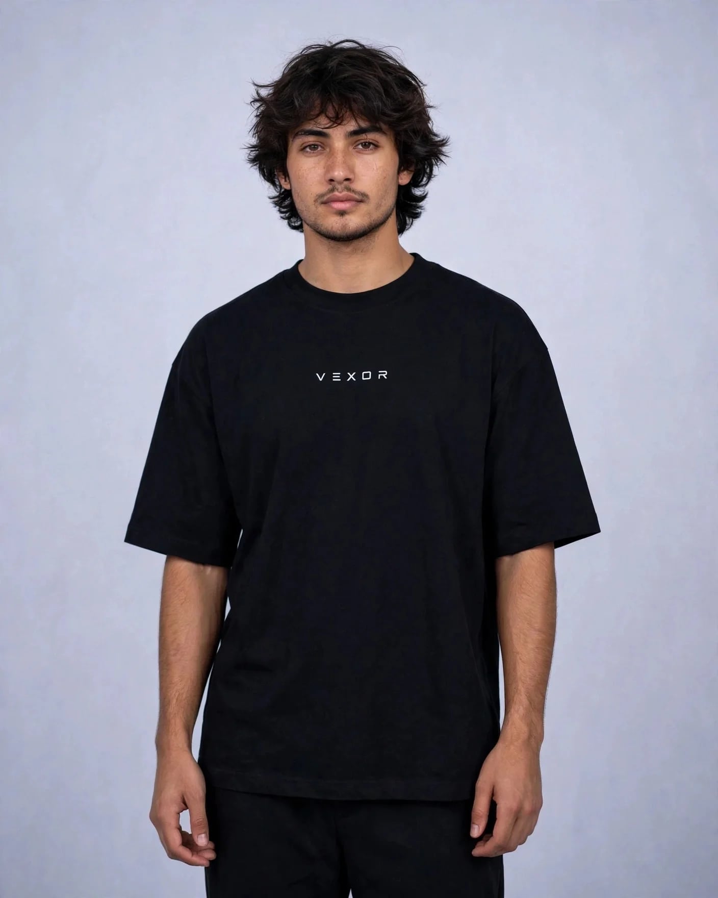Man wearing the black oversized tee, front view with the small white VEXOR wordmark on the chest