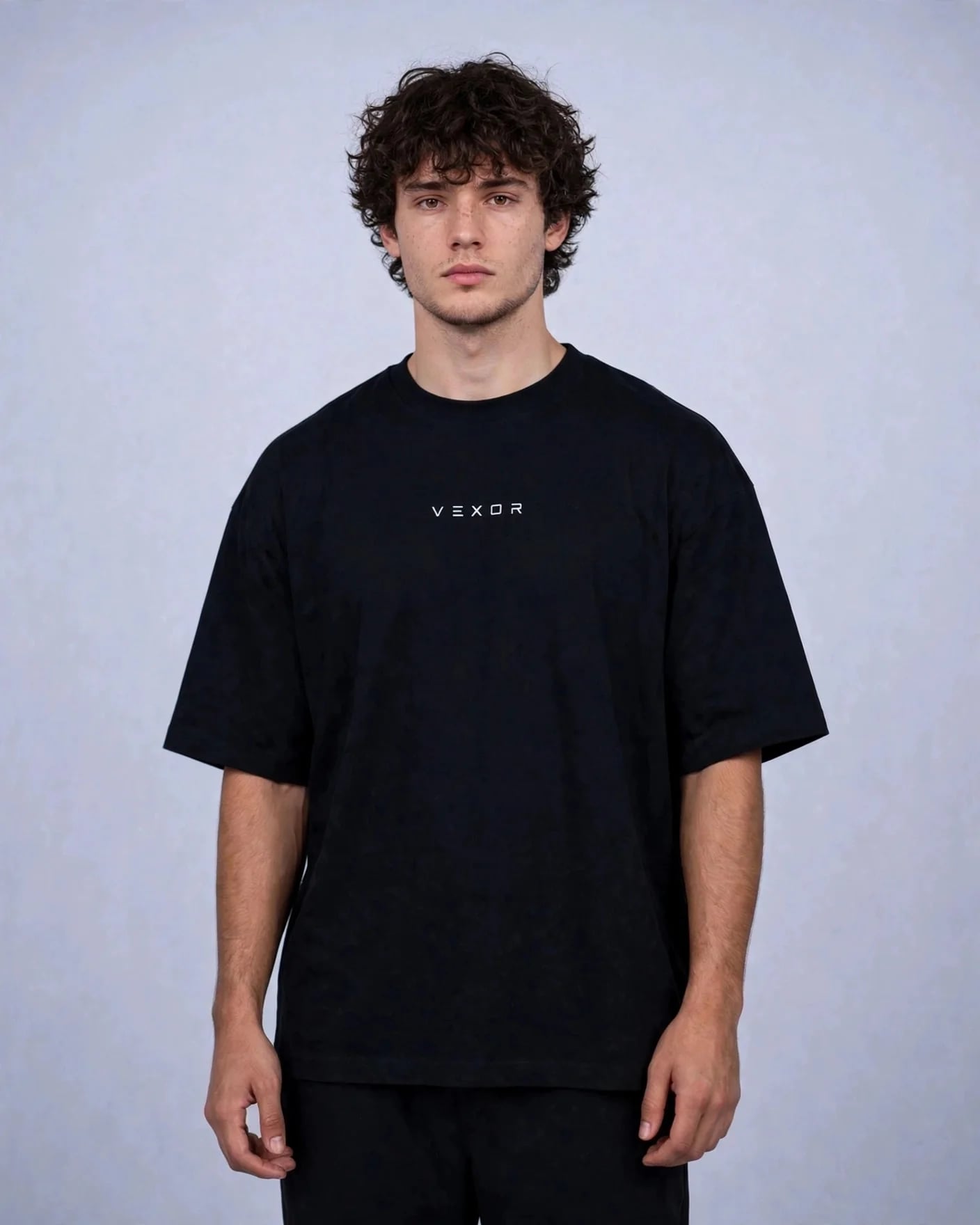 Man wearing the black oversized tee, front view with the small white VEXOR wordmark on the chest
